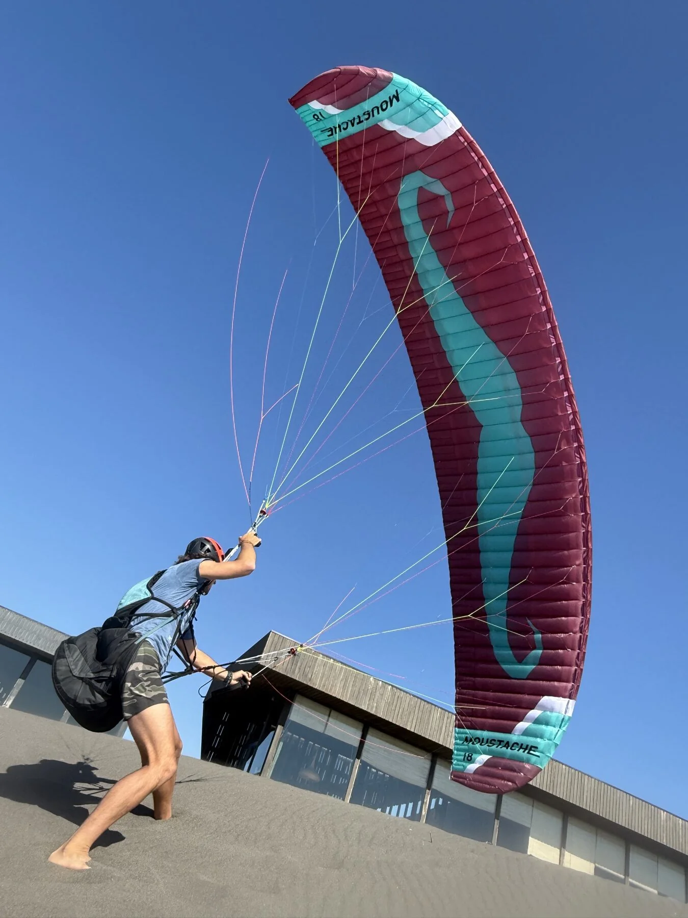 Piloto practicando control de una vela Moustache en arena bajo cielo despejado