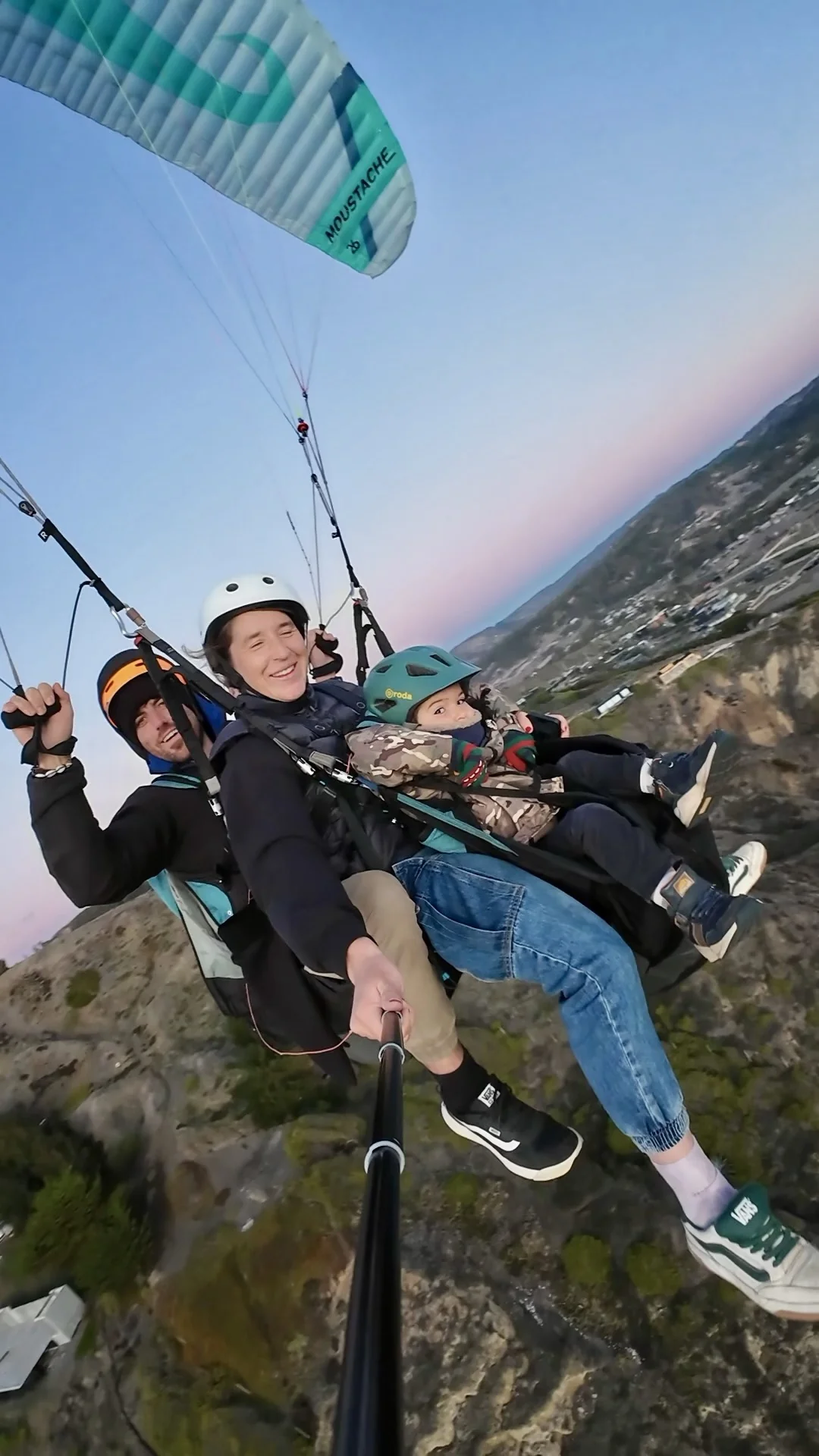 Un niño vuela en parapente tándem junto al piloto y su madre sobre los cerros de Santiago