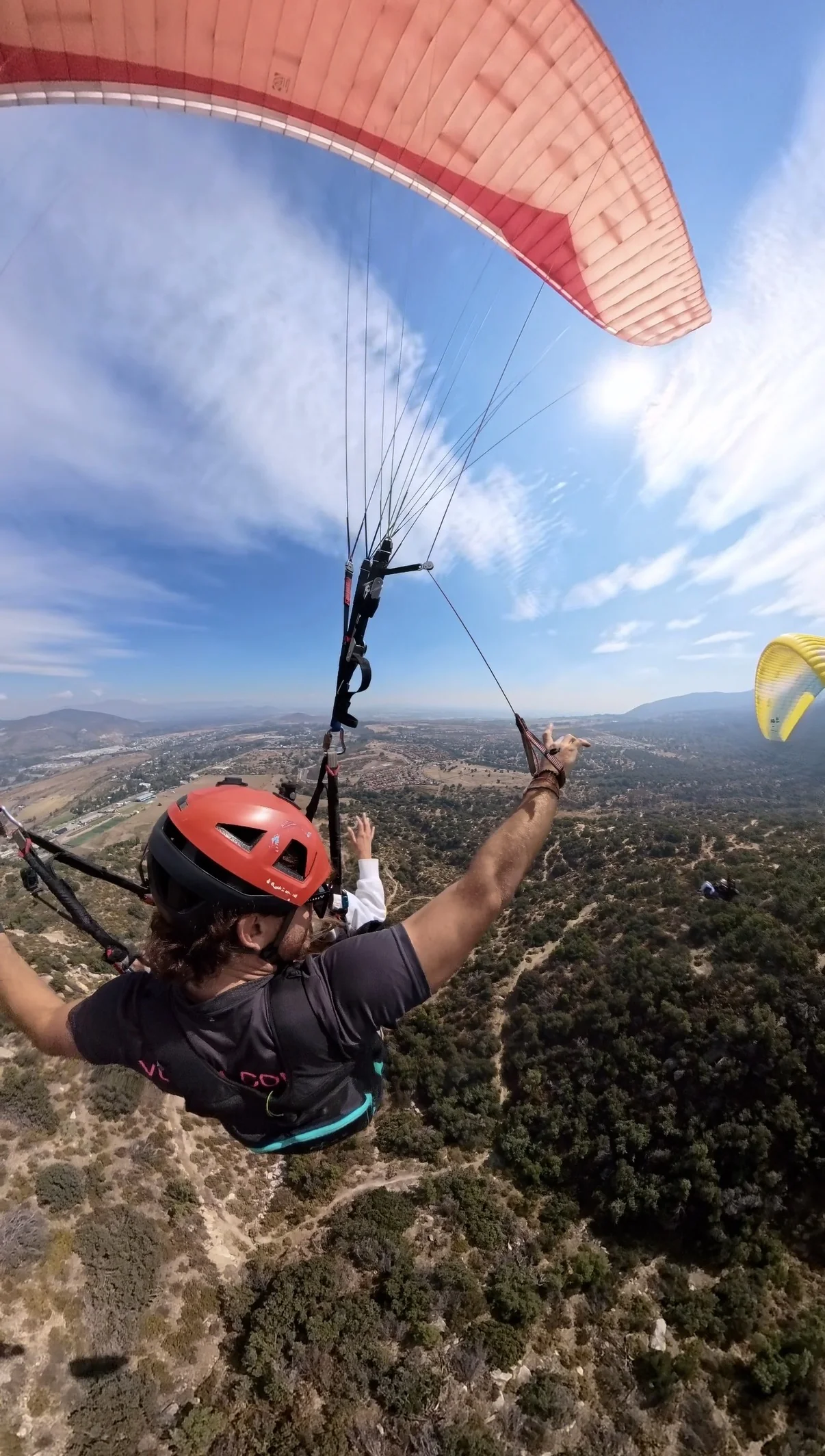 Piloto y pasajera vuelan en parapente con los brazos abiertos, sensación serena de flotar sobre el valle en Santiago